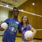 two girls playing and holding volleyball in a gym