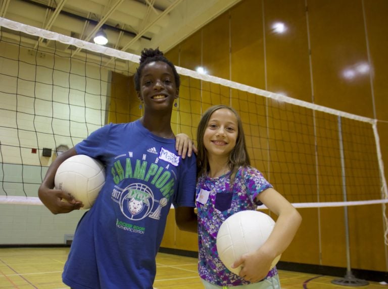 two girls playing and holding volleyball in a gym
