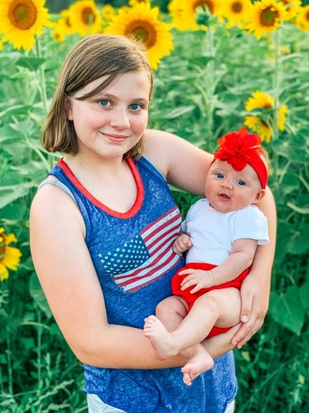 girl holding young infant girl in Sunflower Fields